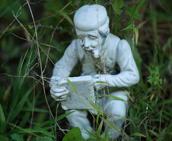 image of statue in green grass of man with pipe writing on a tablet
